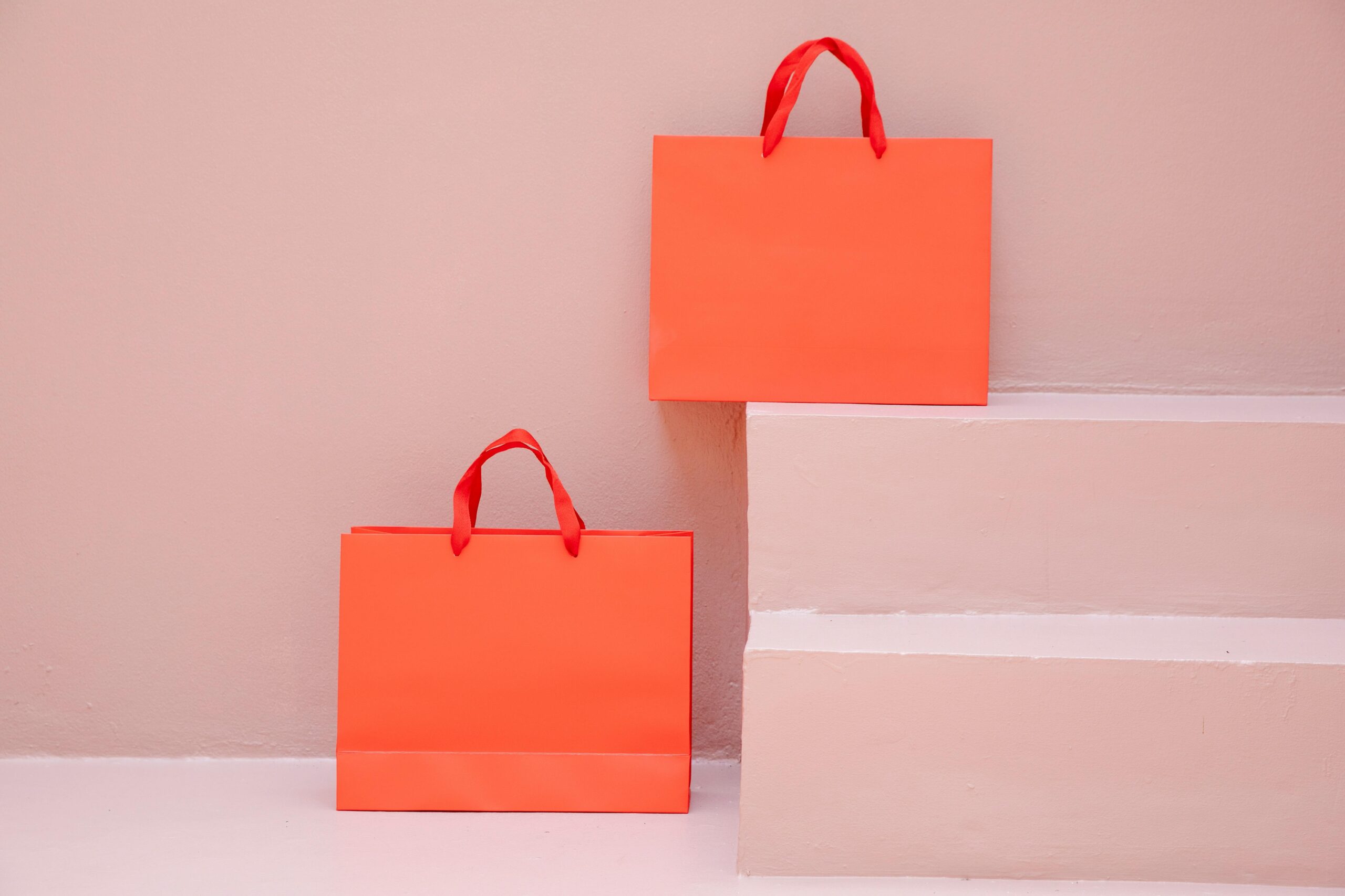 Bright orange shopping bags juxtaposed against pastel steps in a minimalist setting.